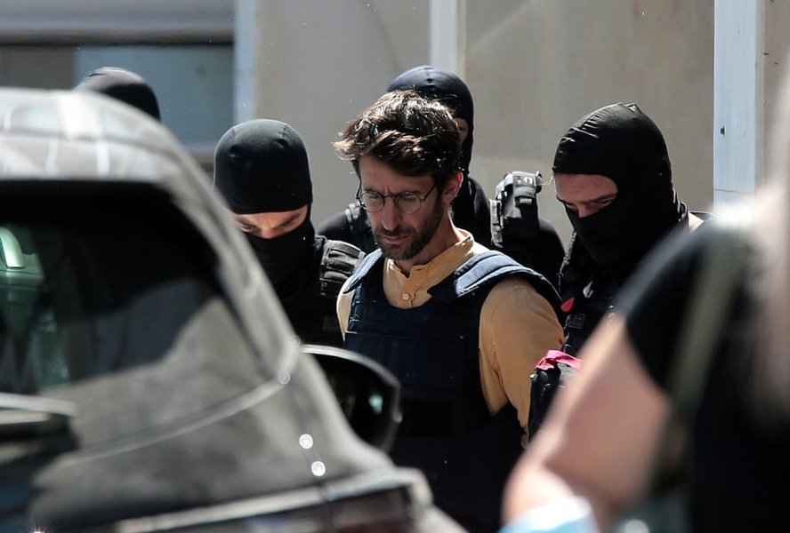 پلیس یکی از دو مظنون متهم به حمله آتشسوزی عمدی به بانک مارفین در ماه مه ۲۰۱۰ را اسکورت میکند..jpeg